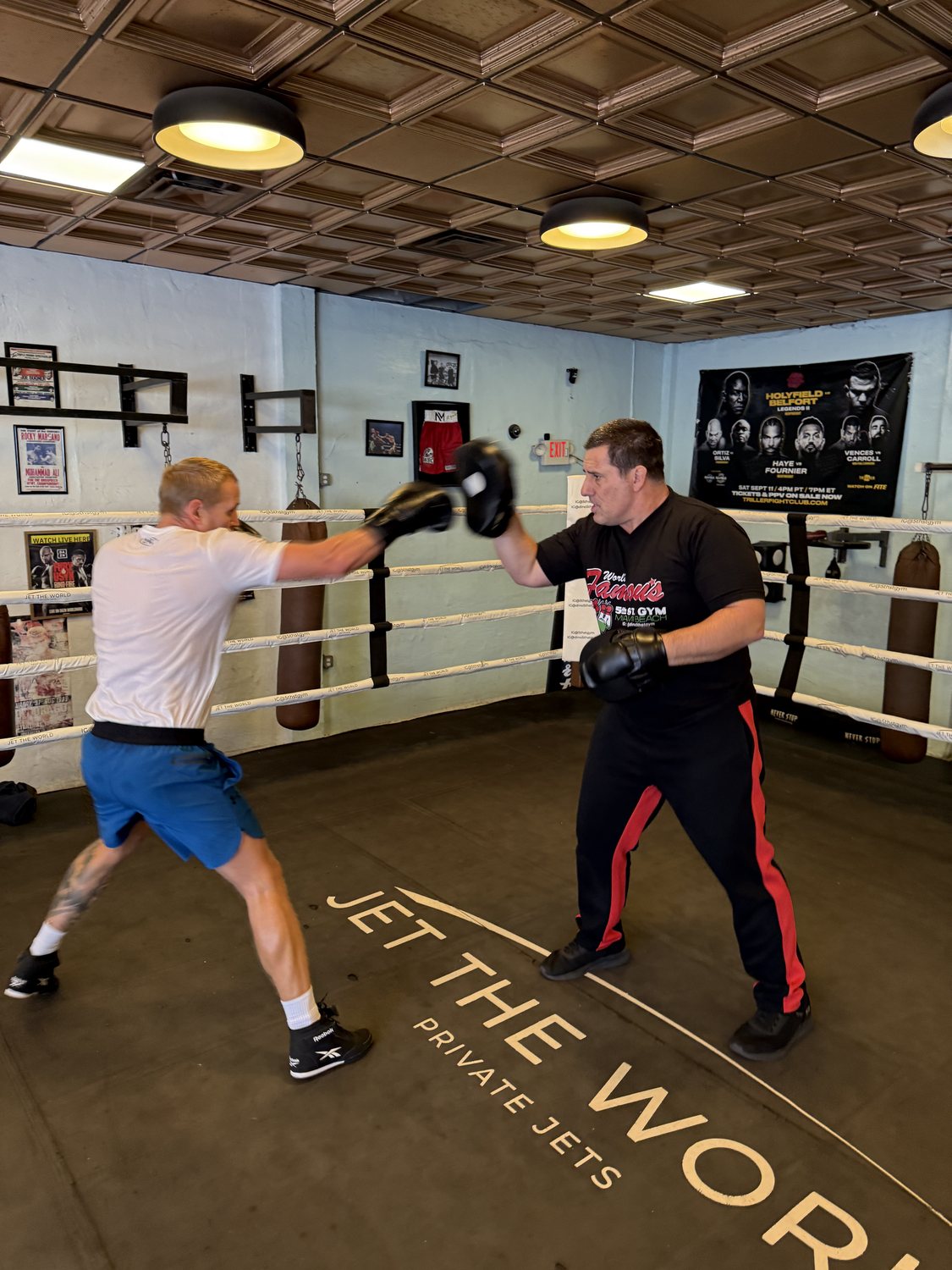 Dino Spencer holding focus mitts in the ring while a client throws a punch.